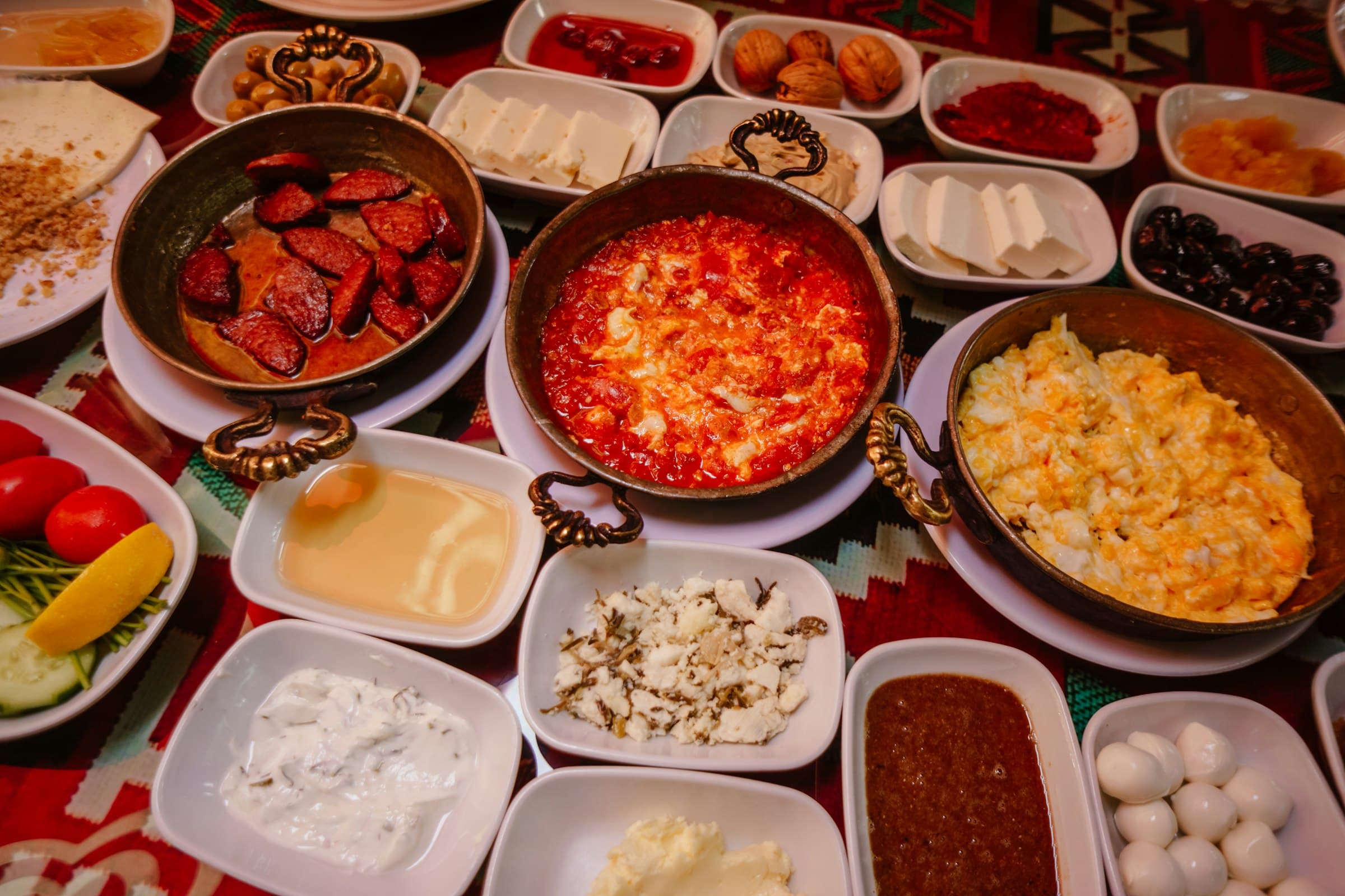 Reich gedeckter türkischer Frühstückstisch mit Menemen, Sucuk, Weißkäse, Oliven und Honig in Kupferpfannen