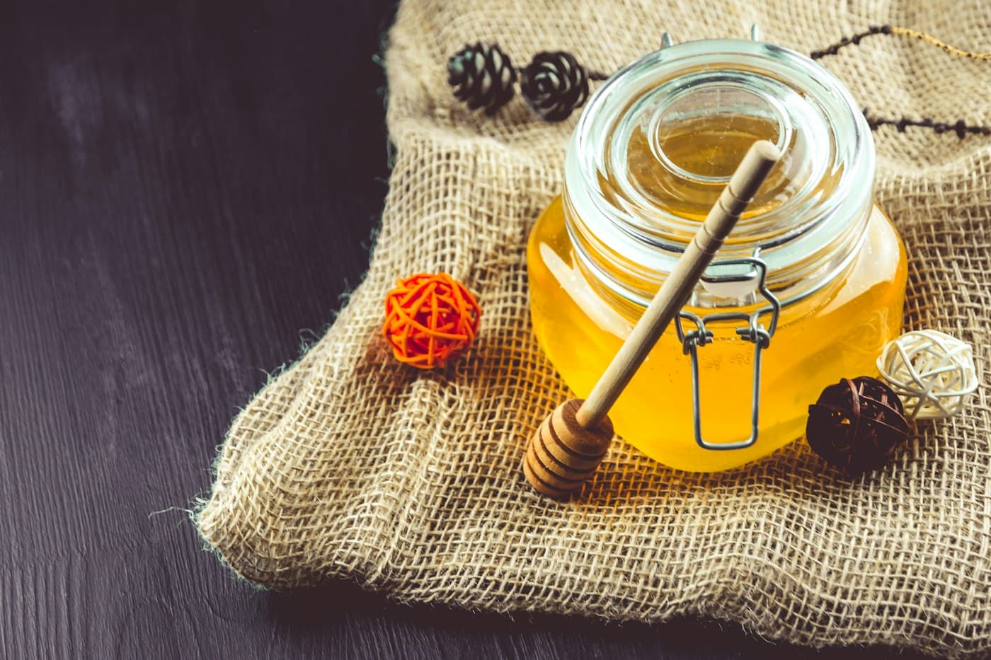 Glas mit goldgelbem Honig und Honiglöffel auf Jutestoff